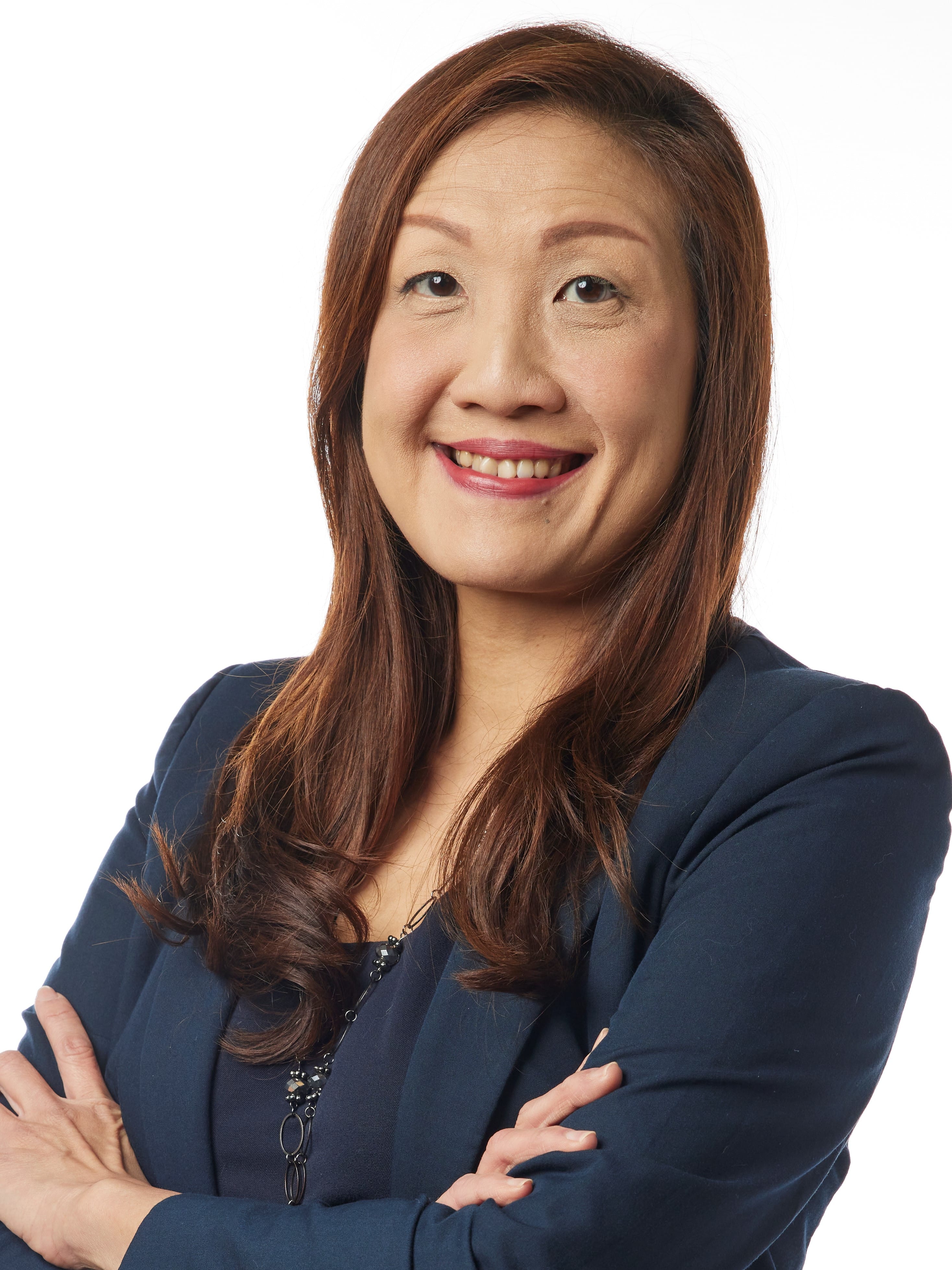 A smiling woman with auburn hair wearing a navy blazer and necklace, arms crossed, against a white background.
