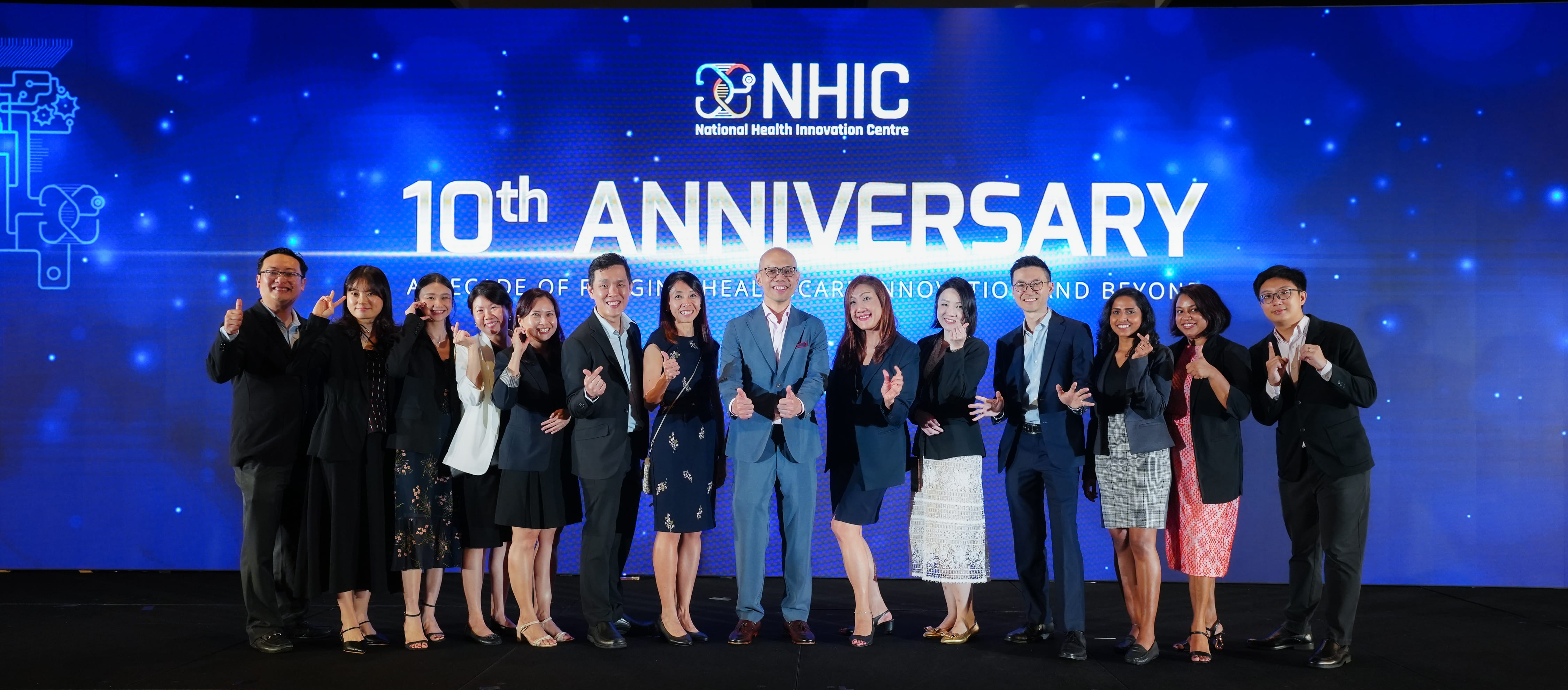 Group of people posing in front of a blue NHIC 10th Anniversary banner at a formal event.