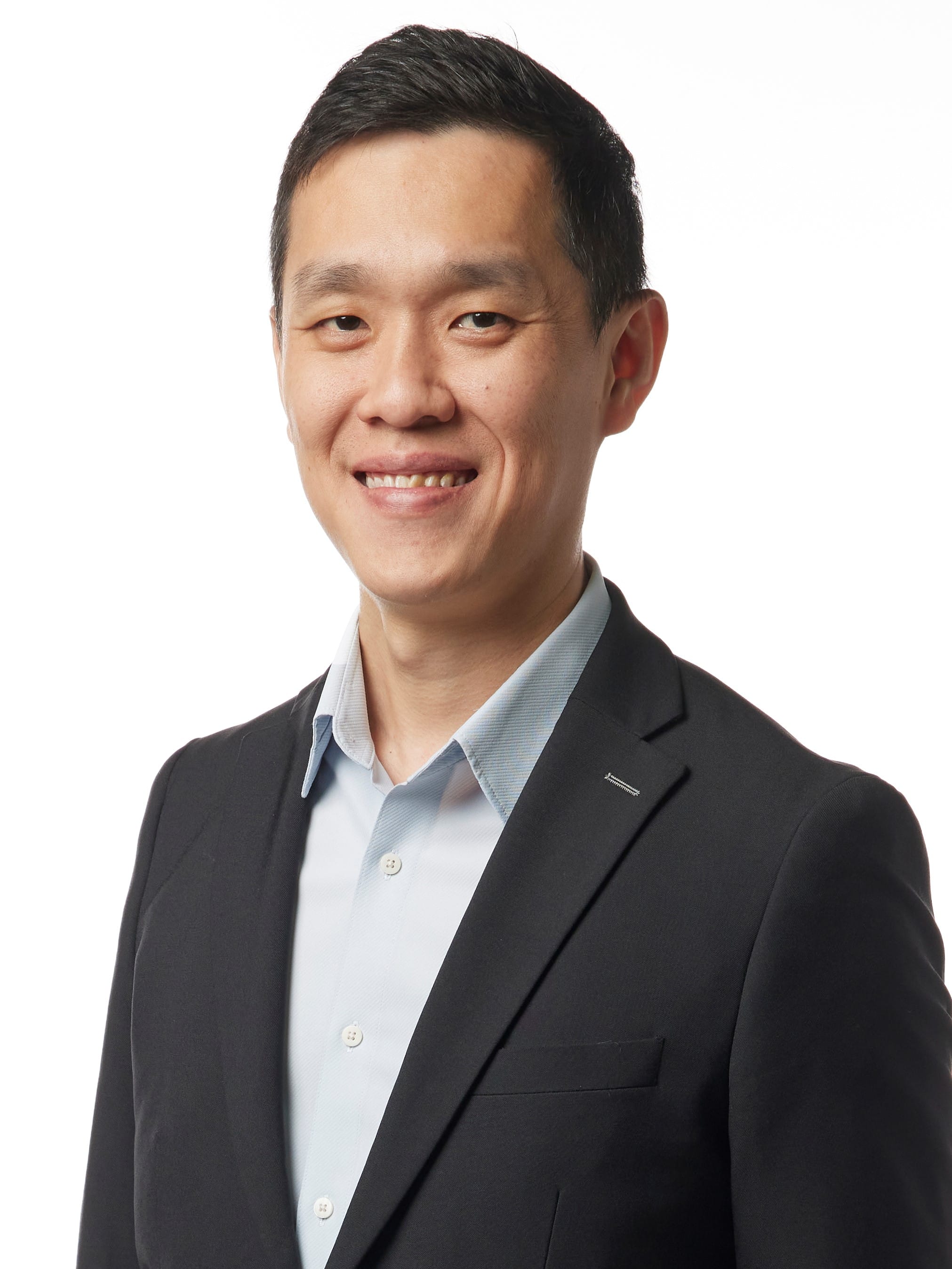 A smiling man with short dark hair wearing a dark blazer and light blue shirt against a white background.