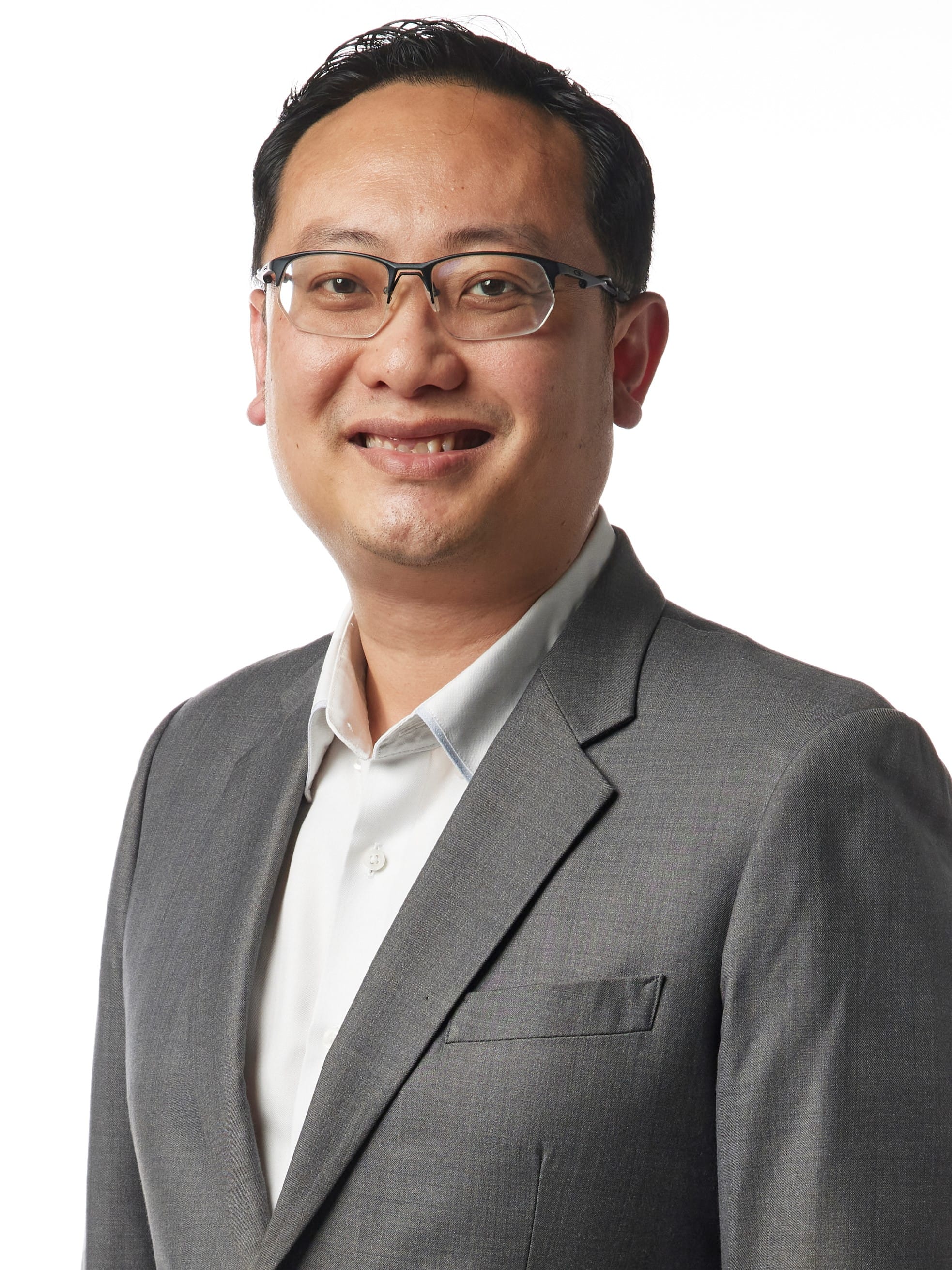 A smiling man wearing glasses, a gray blazer, and a white shirt poses against a white background.