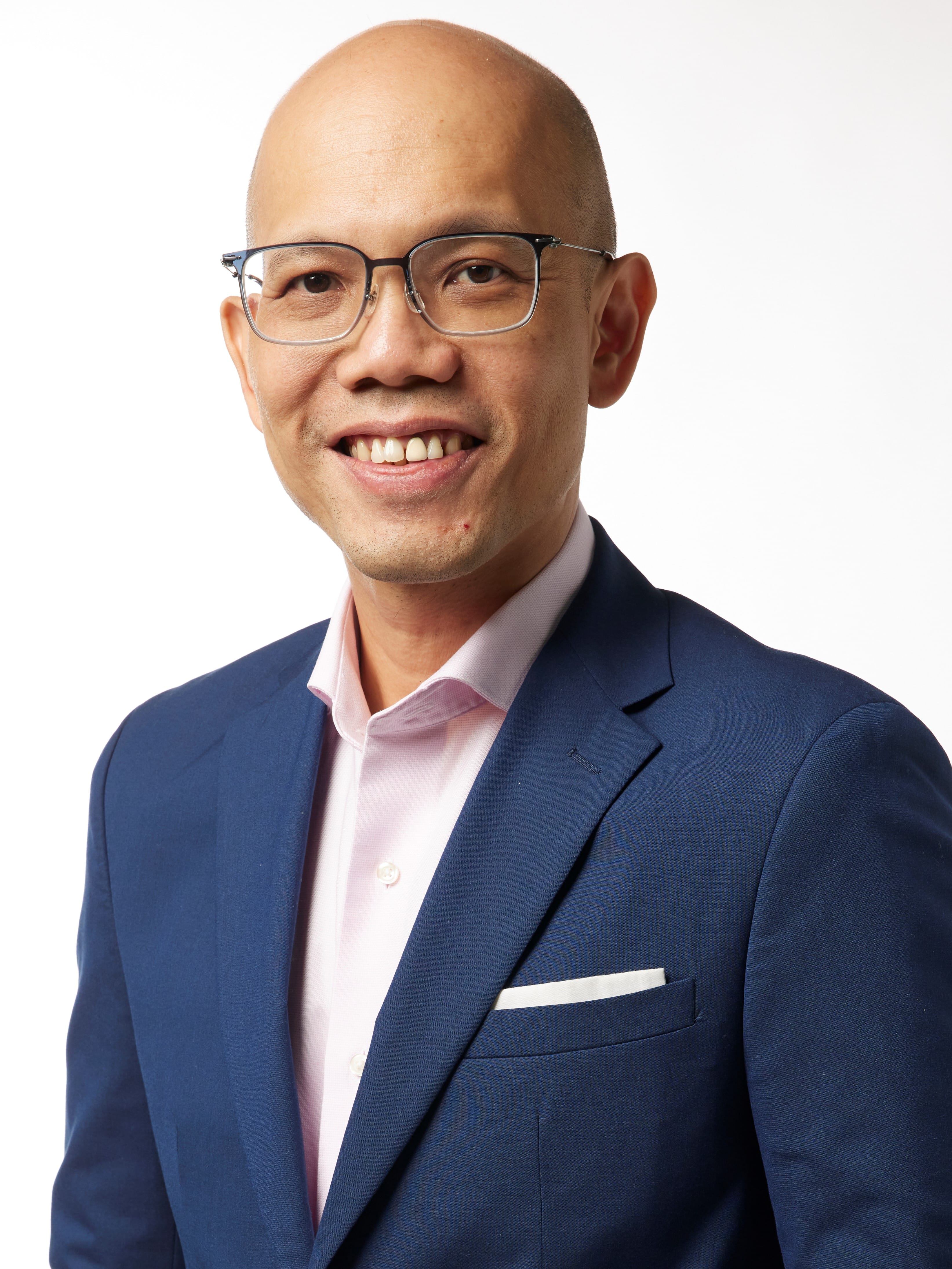Smiling bald man with glasses wearing a blue blazer and pink shirt against a white background.
