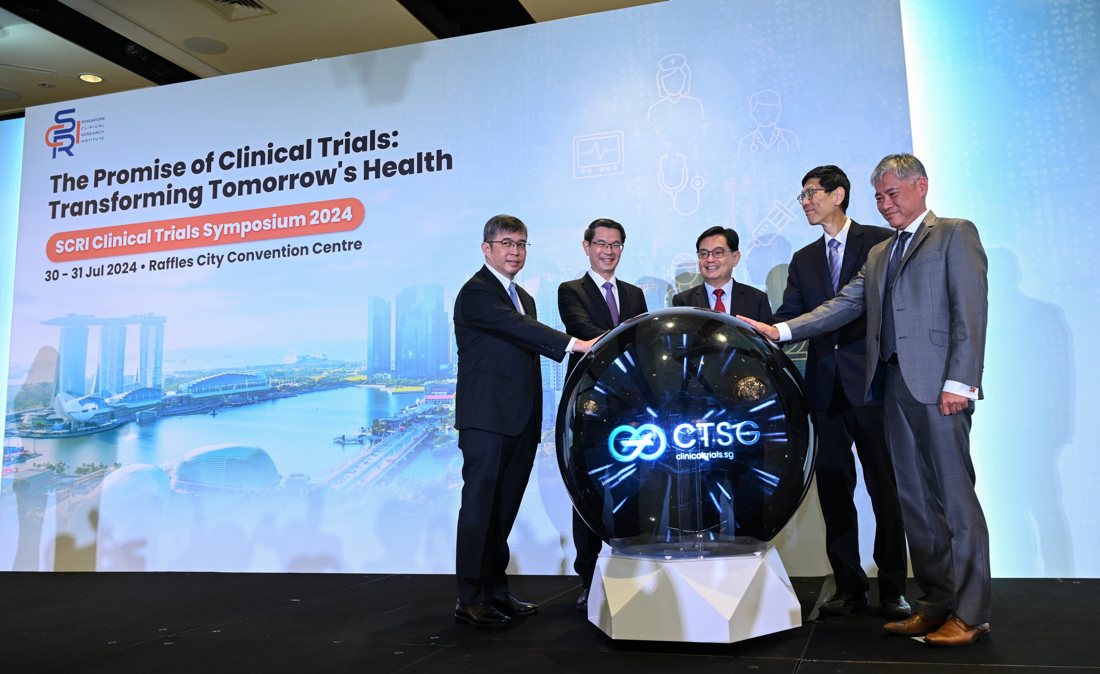 Five men in suits place hands on a glowing CTSG sphere at the SCRI Clinical Trials Symposium 2024 launch event.