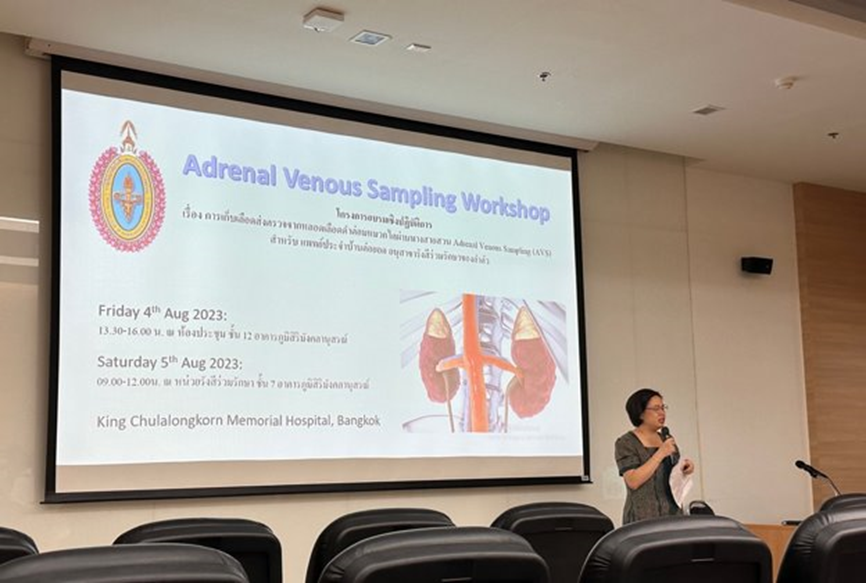 A woman speaks at a podium beside a projected slide for an Adrenal Venous Sampling Workshop in Bangkok, August 2023.