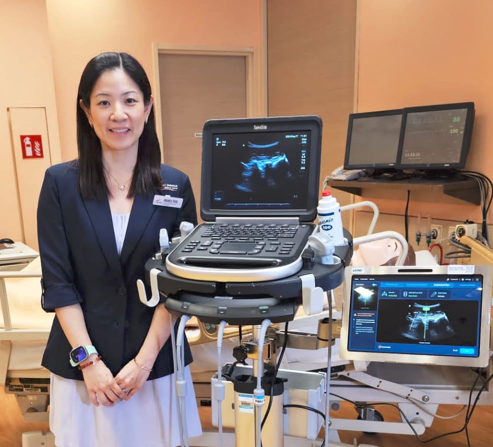 A woman in a dark blazer stands beside a SonoSite ultrasound machine in a medical room.