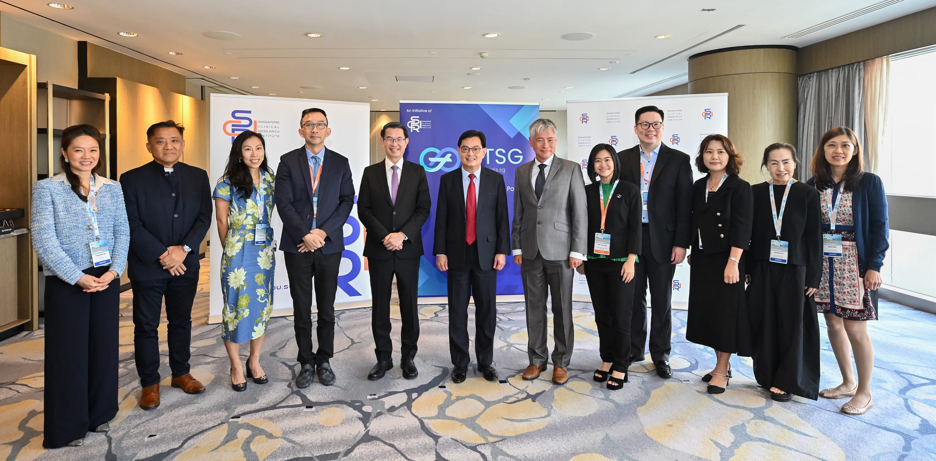 A group of twelve professionals posing in front of Singapore Clinical Research Institute banners at a formal event.