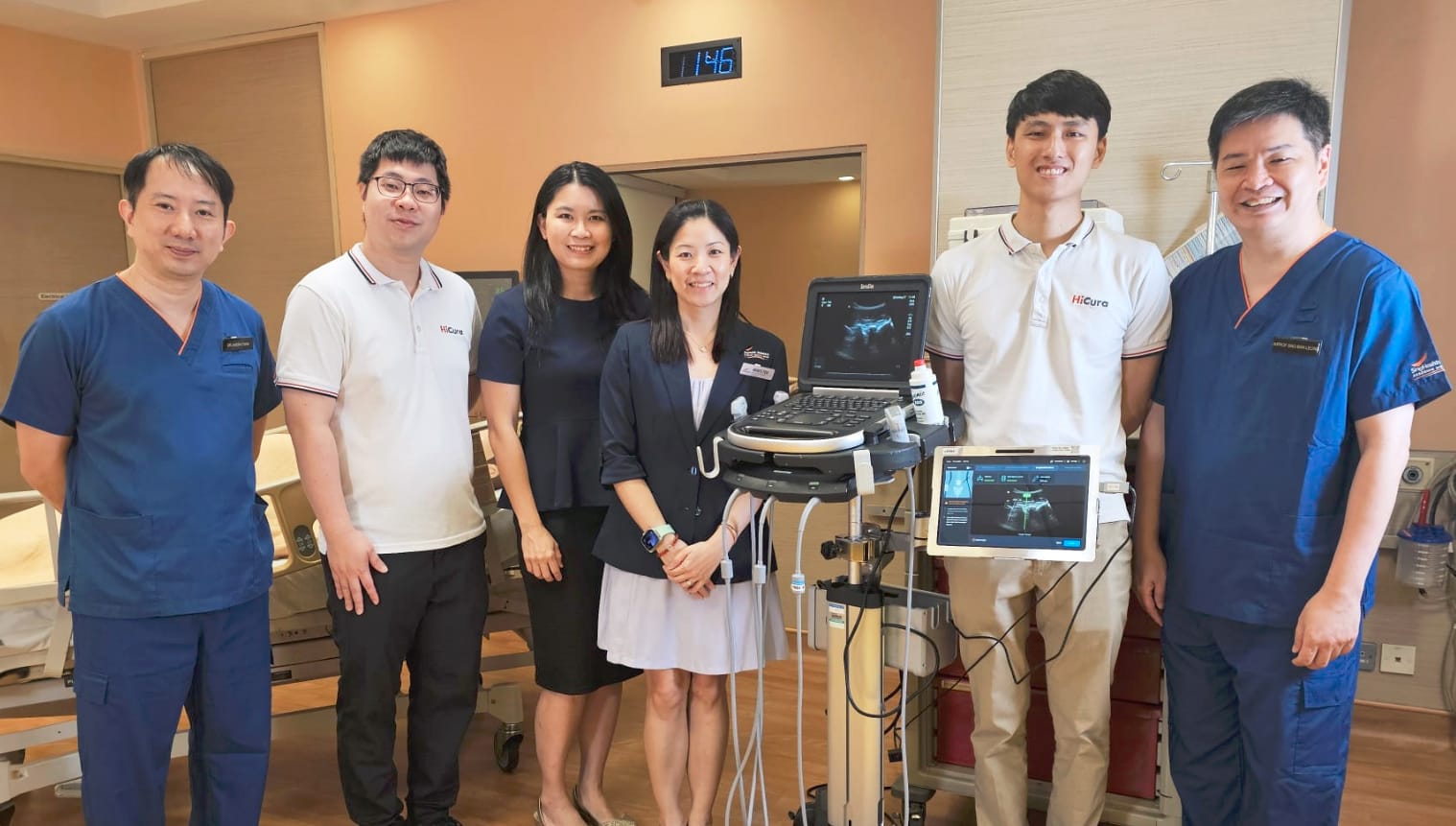 Six people smiling in a hospital room beside an ultrasound machine, two wearing blue scrubs and two in HiCura shirts.