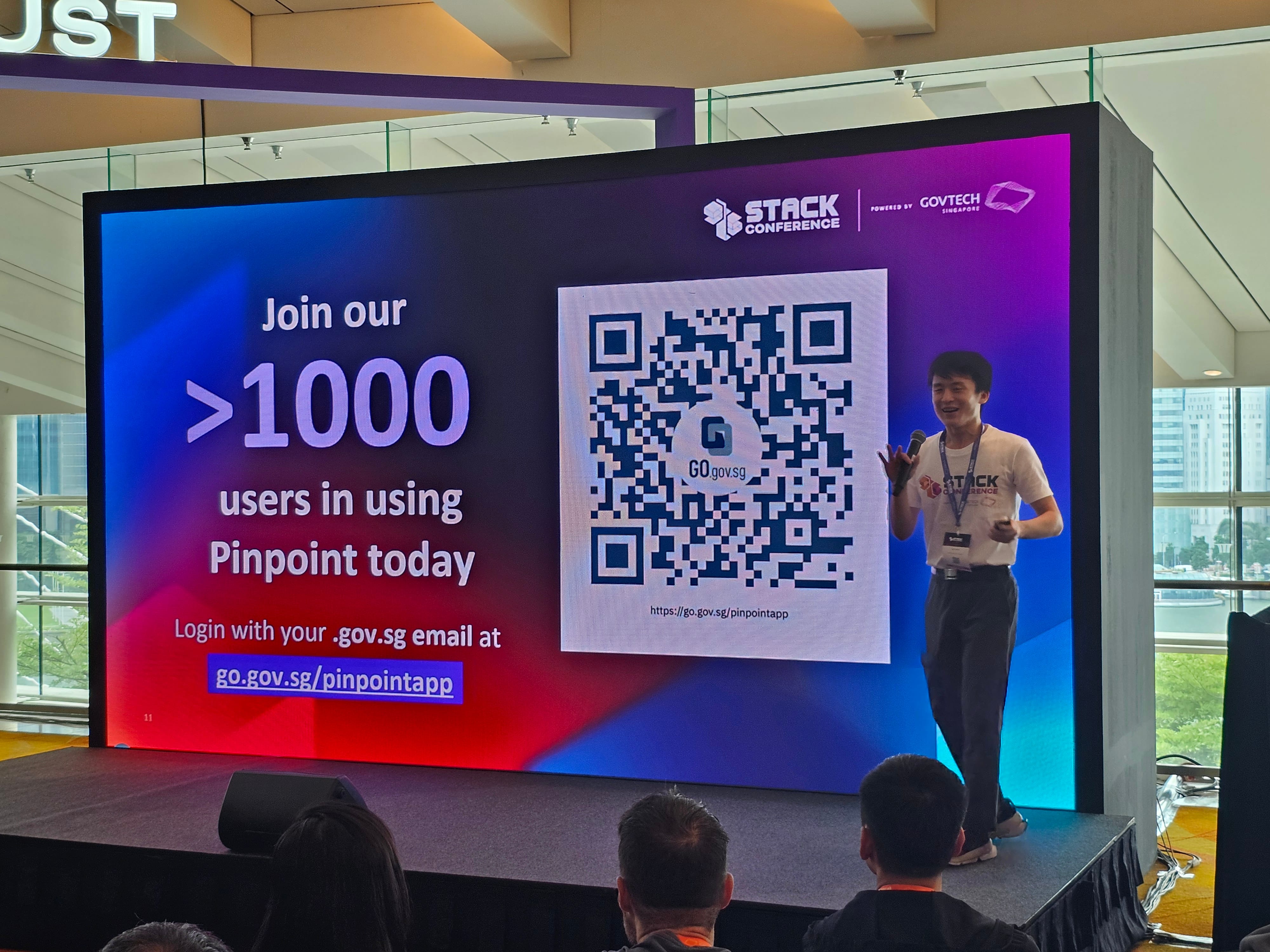A speaker presents at STACK Conference by GovTech, standing beside a slide promoting Pinpoint app with a QR code.