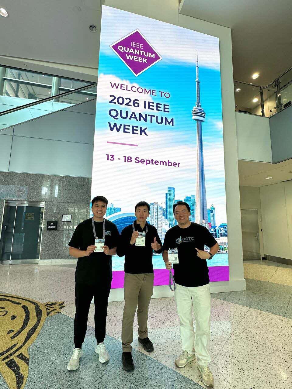 Three DOTC attendees at the 2026 IEEE Quantum Week welcome sign in Toronto.