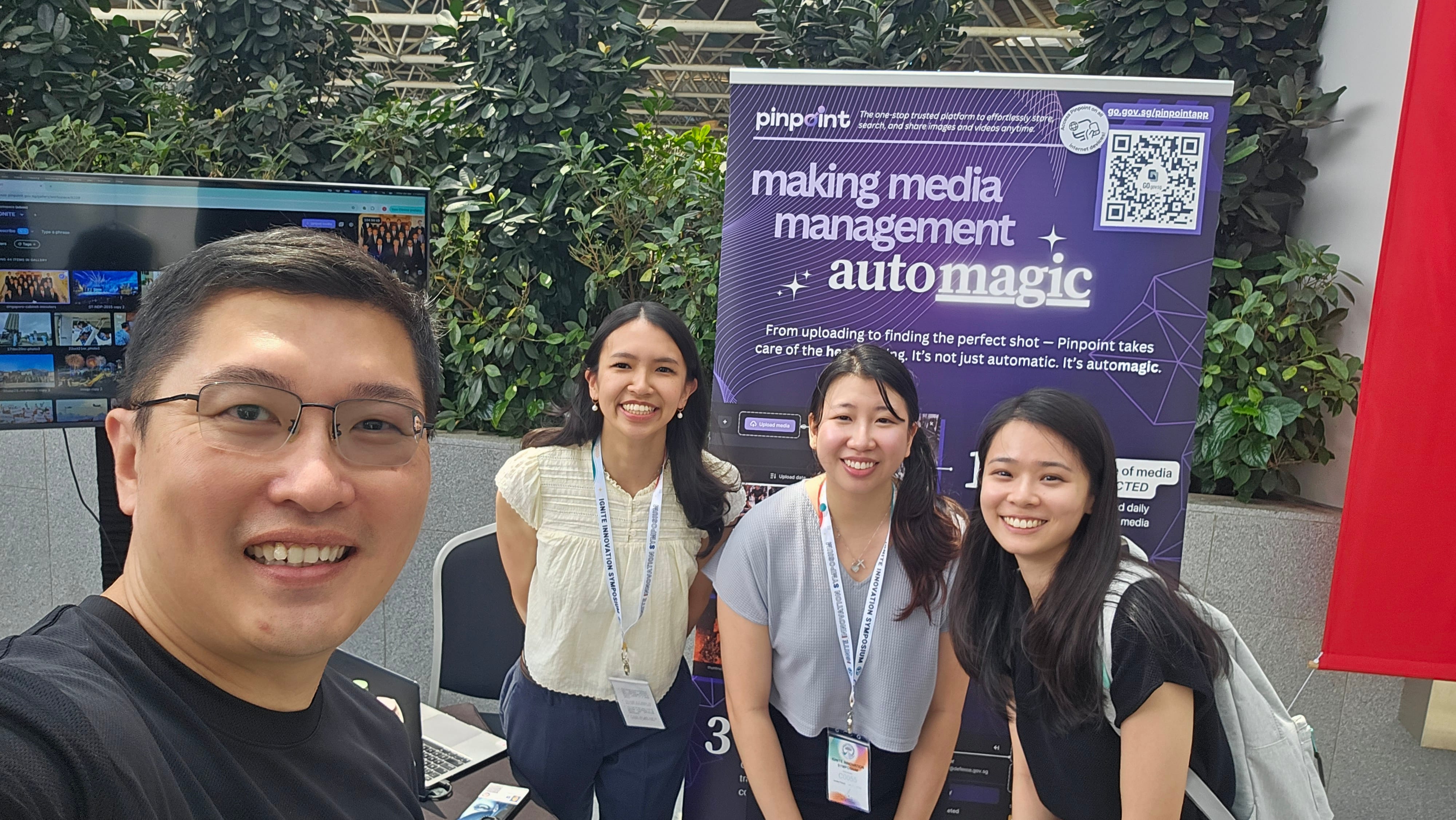 Four smiling people pose in front of a purple Pinpoint banner reading "making media management automagic" at an event.