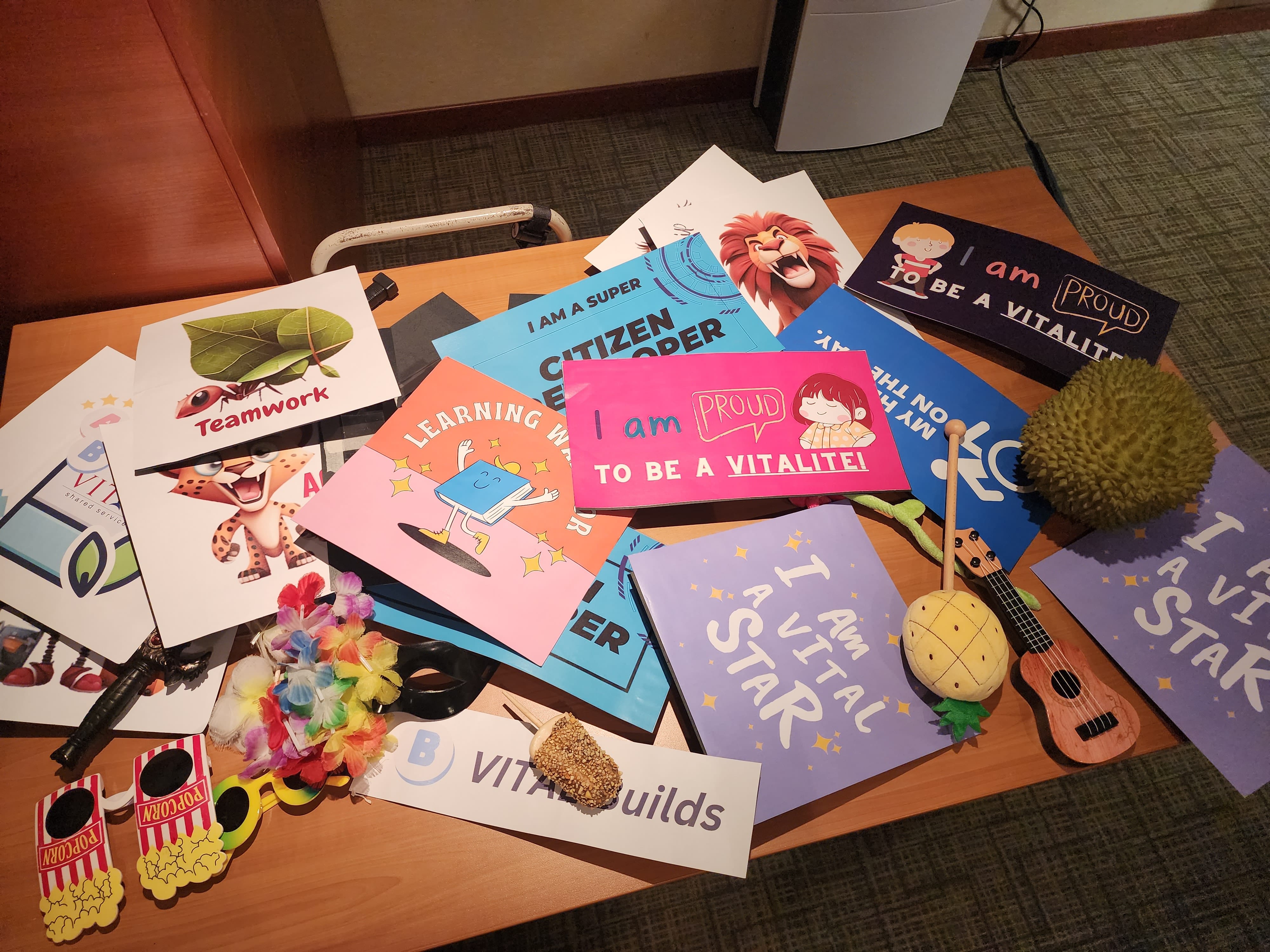 Colorful motivational cards, a ukulele, durian, toy maracas, and novelty glasses spread on a wooden table.