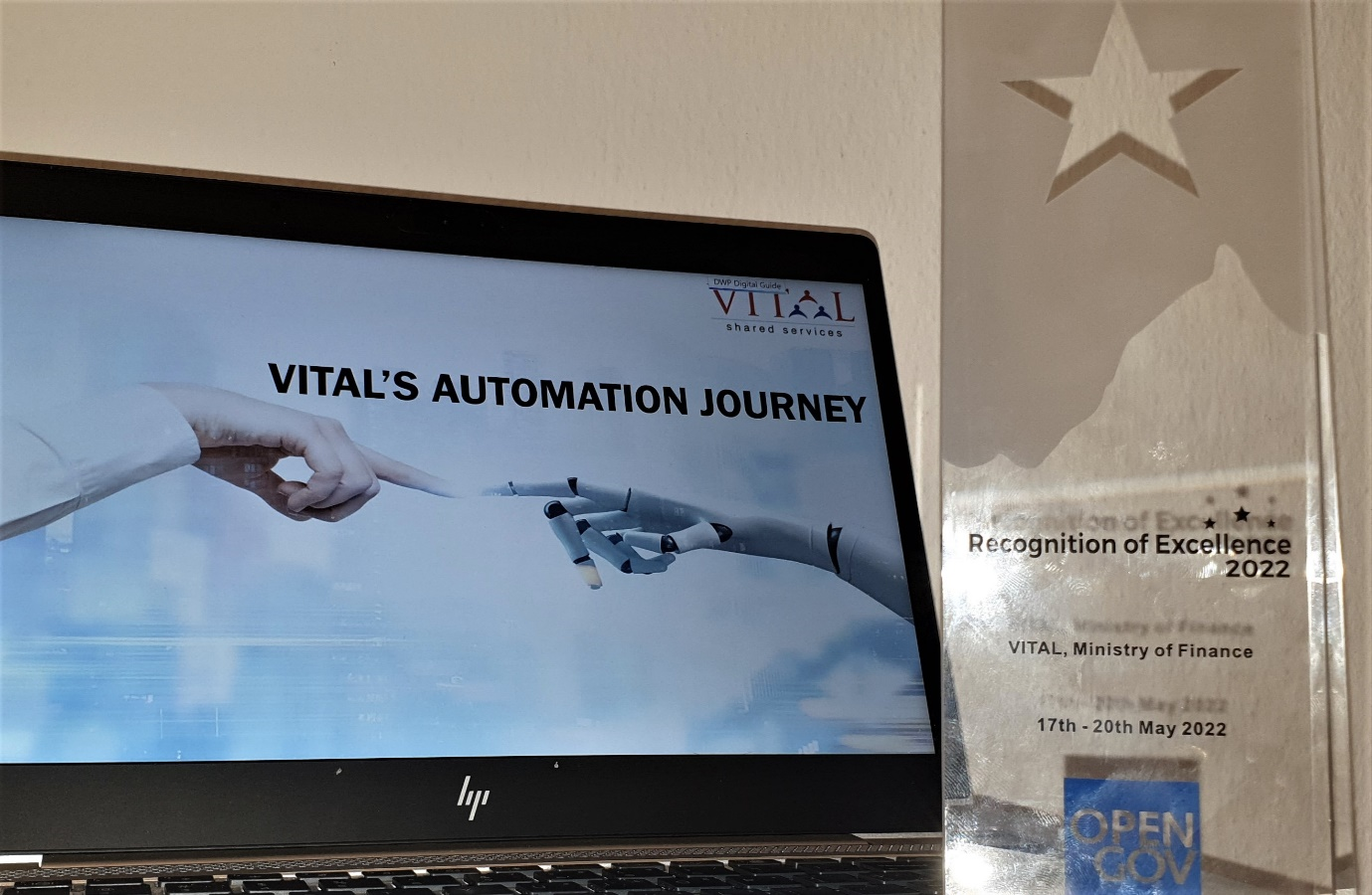 Laptop showing a VITAL automation journey slide beside a Recognition of Excellence 2022 glass award trophy.