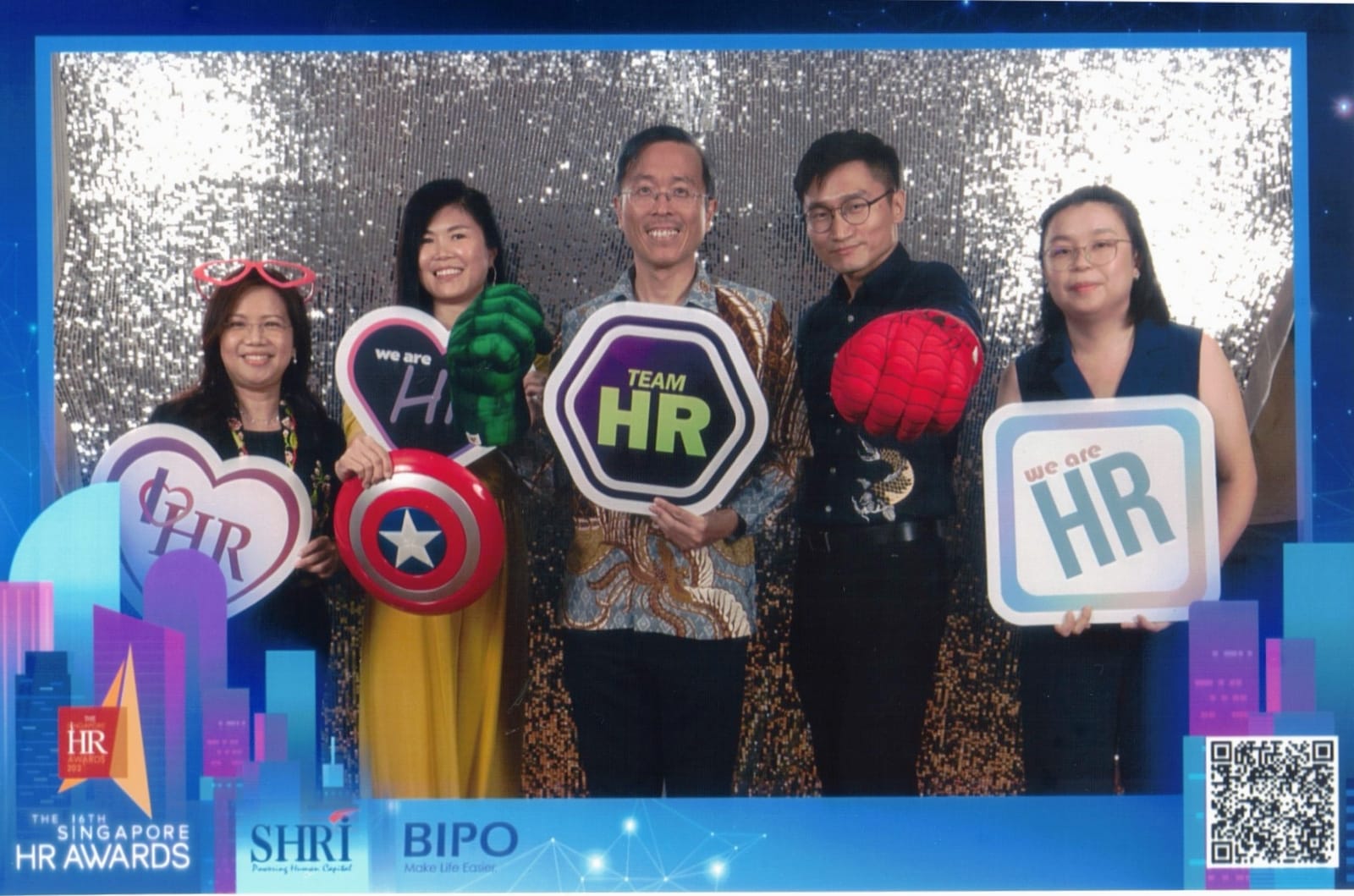 Five people pose at the Singapore HR Awards photo booth holding HR-themed signs and superhero props.