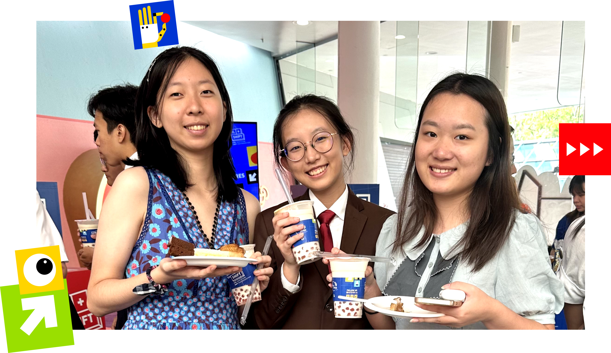Three smiling young women hold drinks and plates of food at an indoor event.
