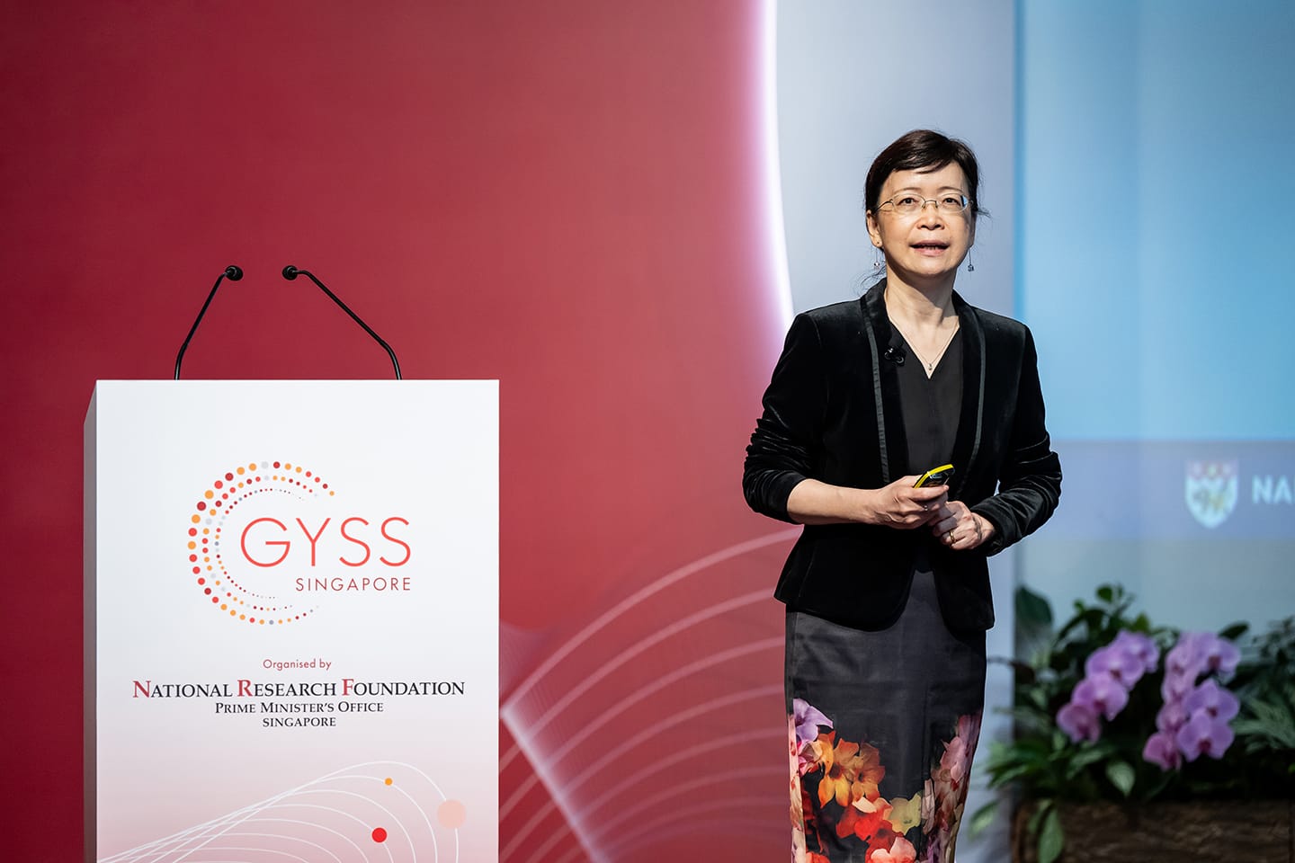 Woman in black blazer speaking at a GYSS Singapore podium organised by the National Research Foundation.