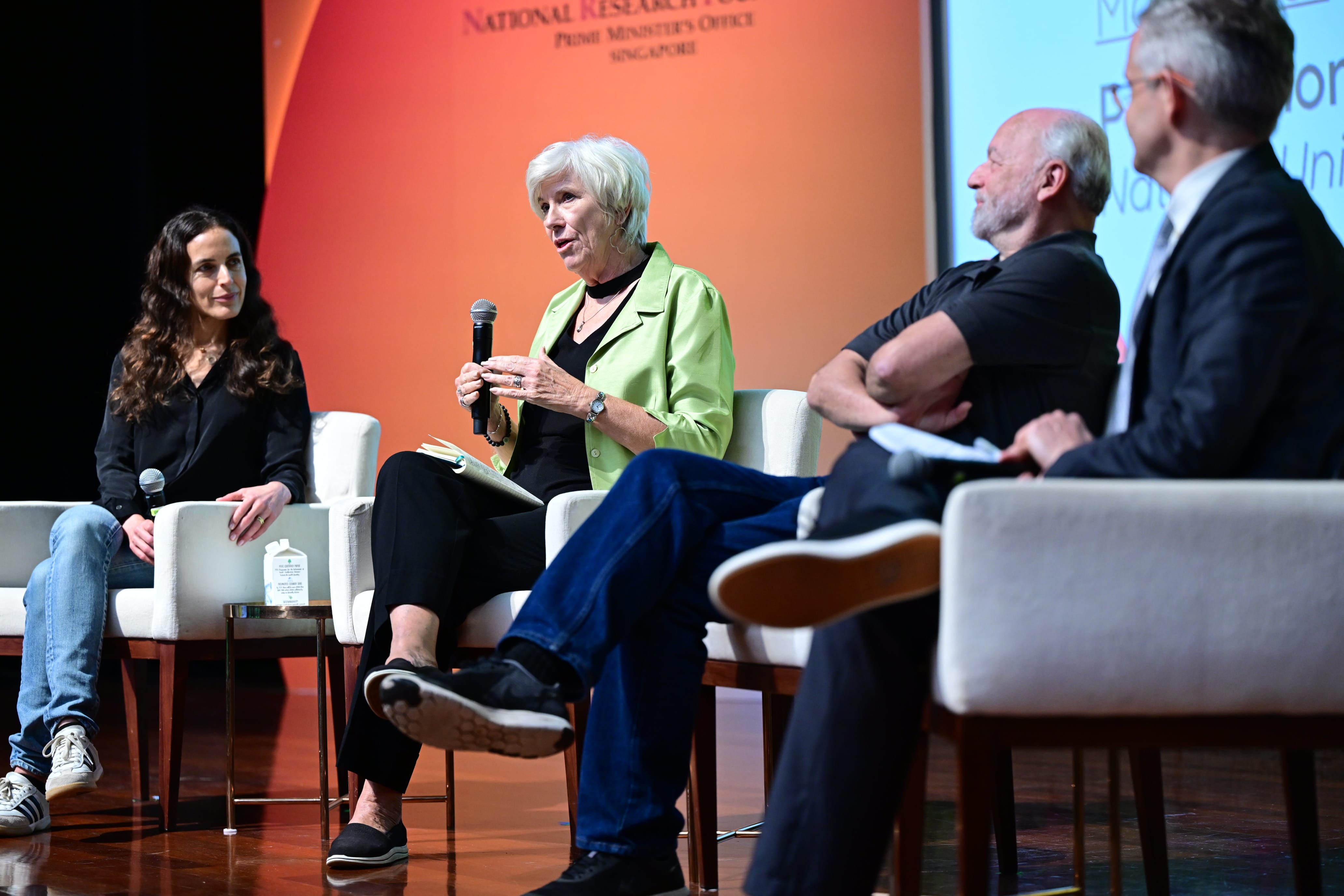 Four panelists seated on stage at a Singapore National Research Foundation event, with a woman speaking into a microphone.