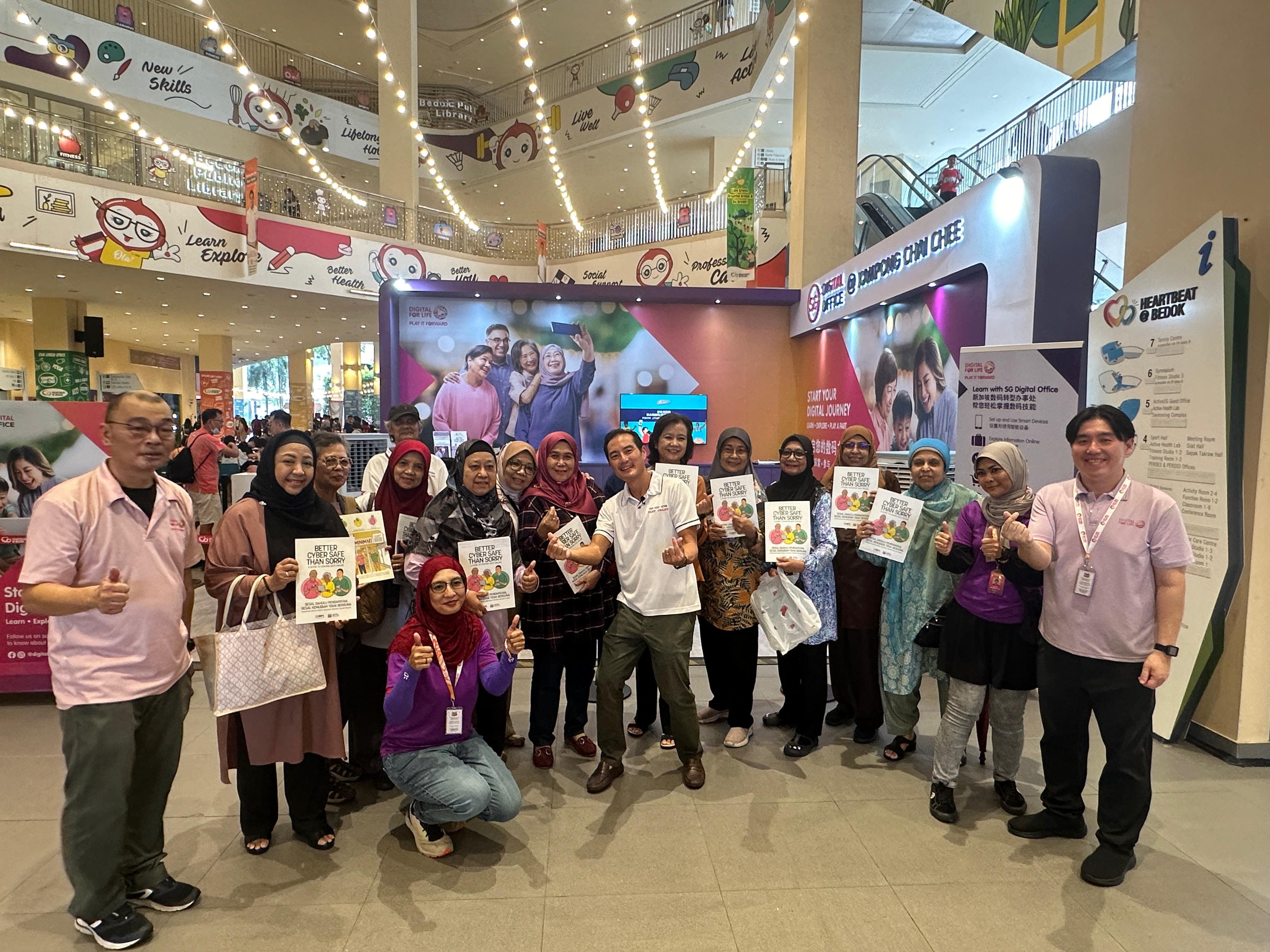 A group of people posing with thumbs up inside a mall, holding pamphlets reading "Better Cyber Safe Than Sorry."