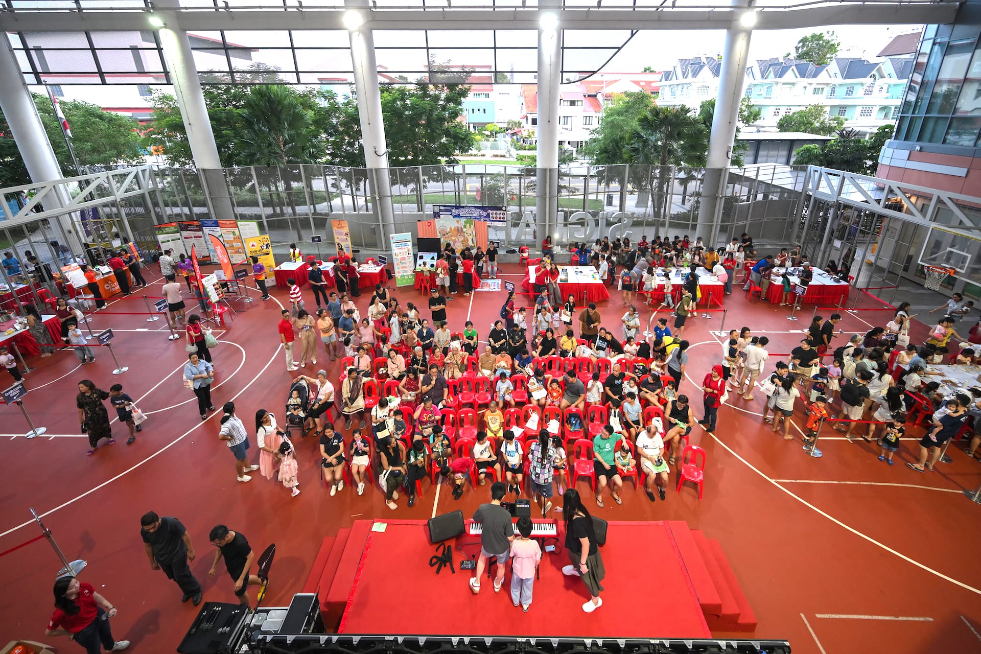 An overhead view of a family day event in a covered basketball court with a stage and red chairs.