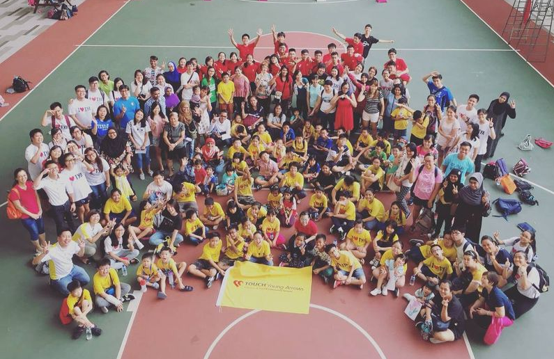 Large group of people posing on an outdoor basketball court, many wearing yellow shirts, with a Touch Young Arrows banner.