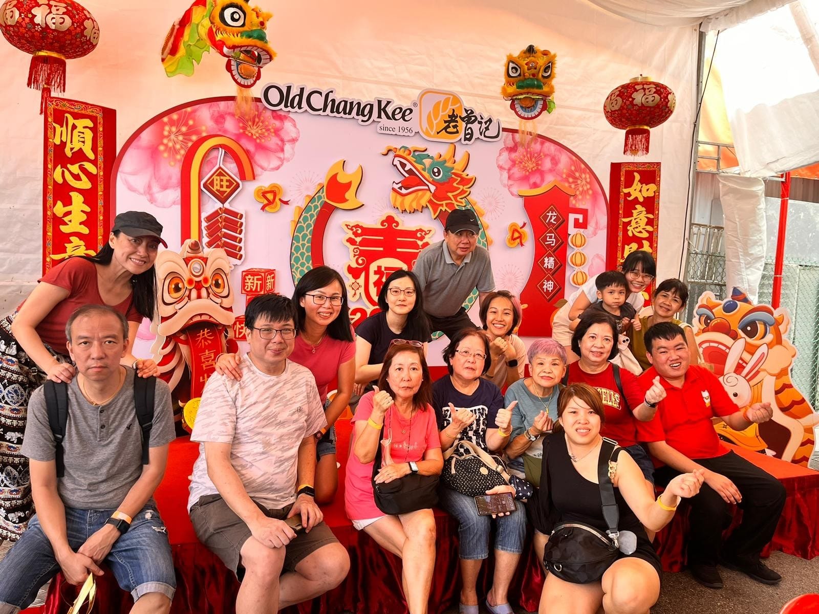 Group of people posing in front of an Old Chang Kee Chinese New Year backdrop with lion heads and red decorations.