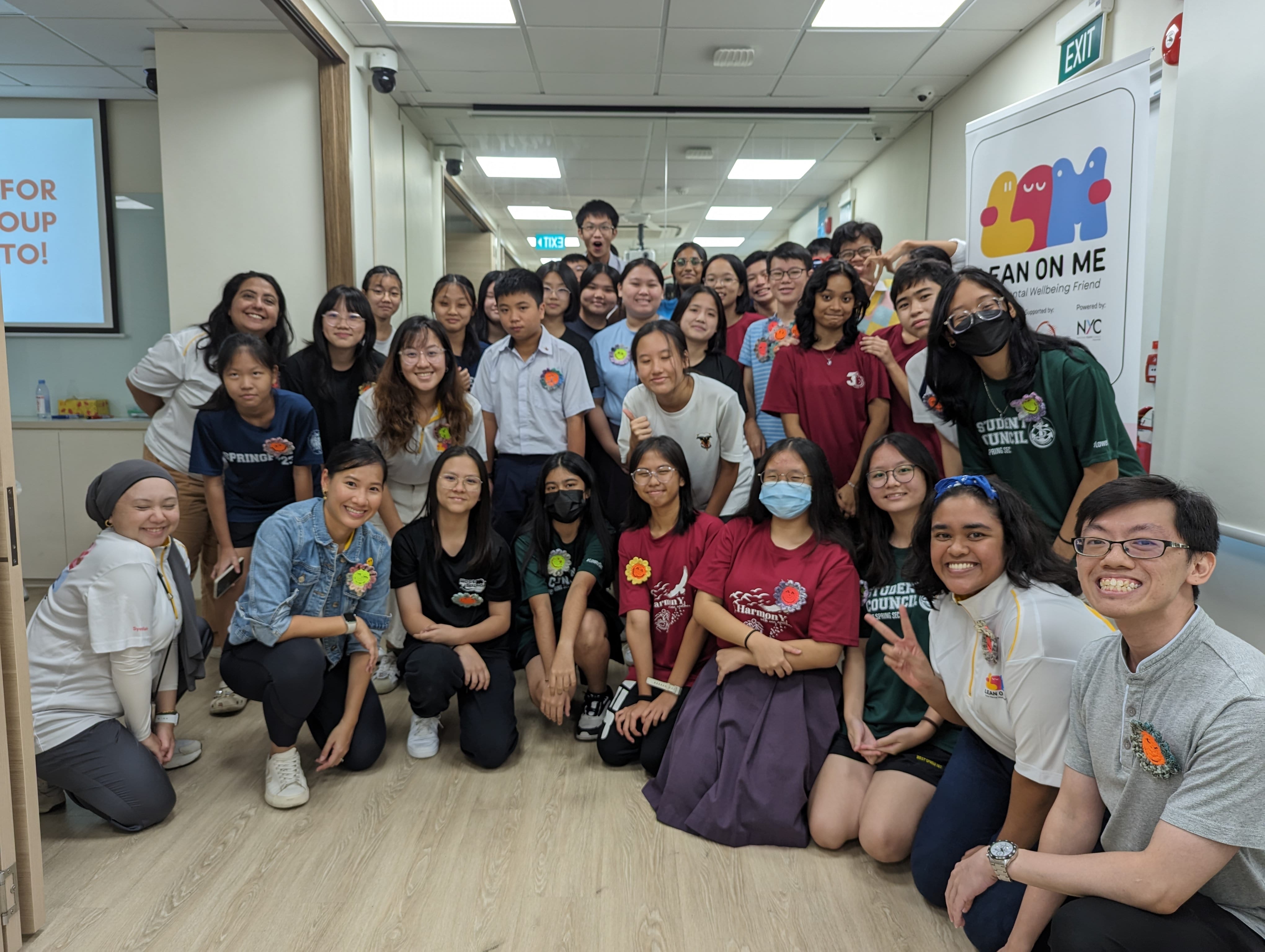 A large group of students and adults posing together in an indoor hallway near a Lean On Me banner.