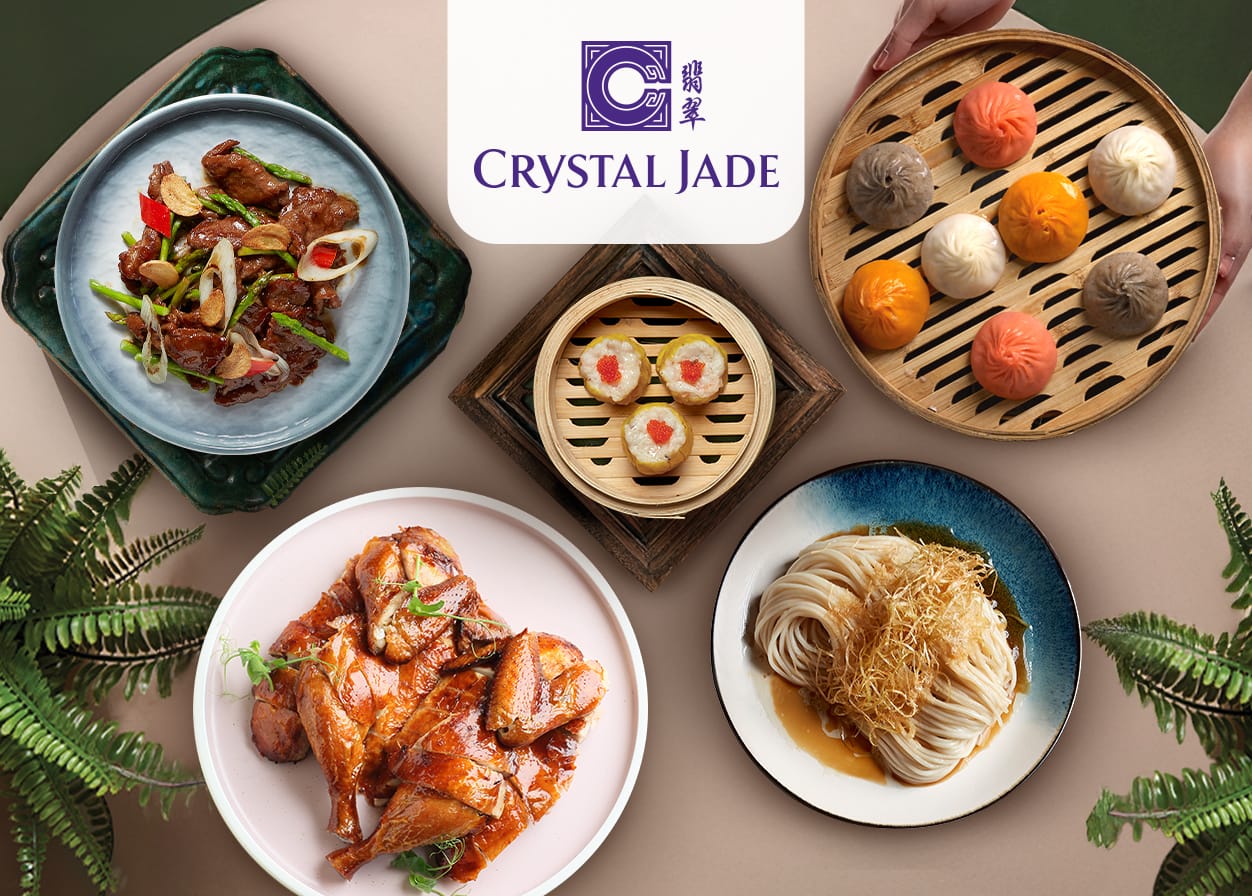Crystal Jade restaurant spread showing dim sum, roasted chicken, noodles, and stir-fried meat on a round table.