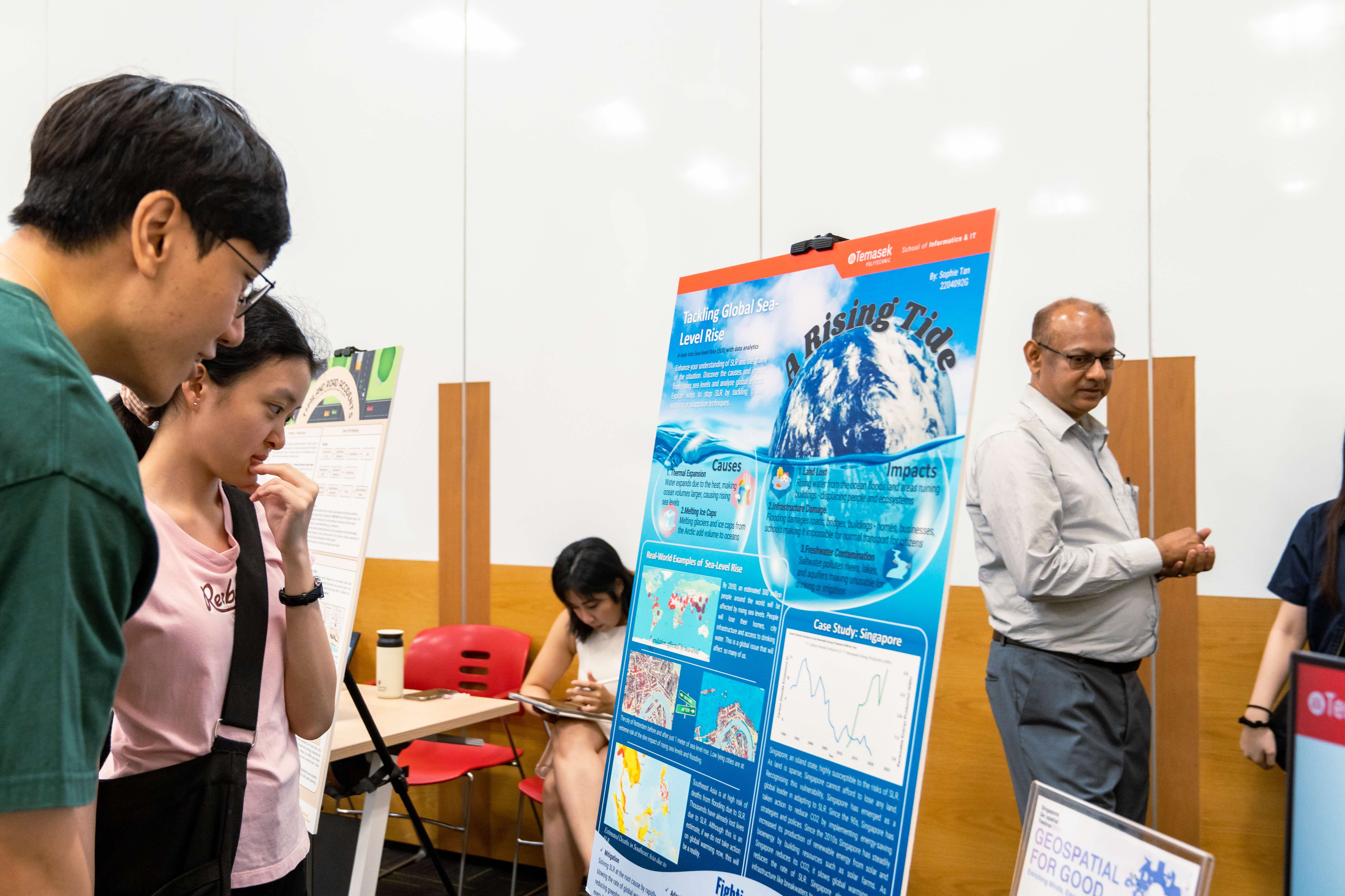 Two students examine a poster titled "A Rising Tide" about tackling global sea-level rise at an academic fair.