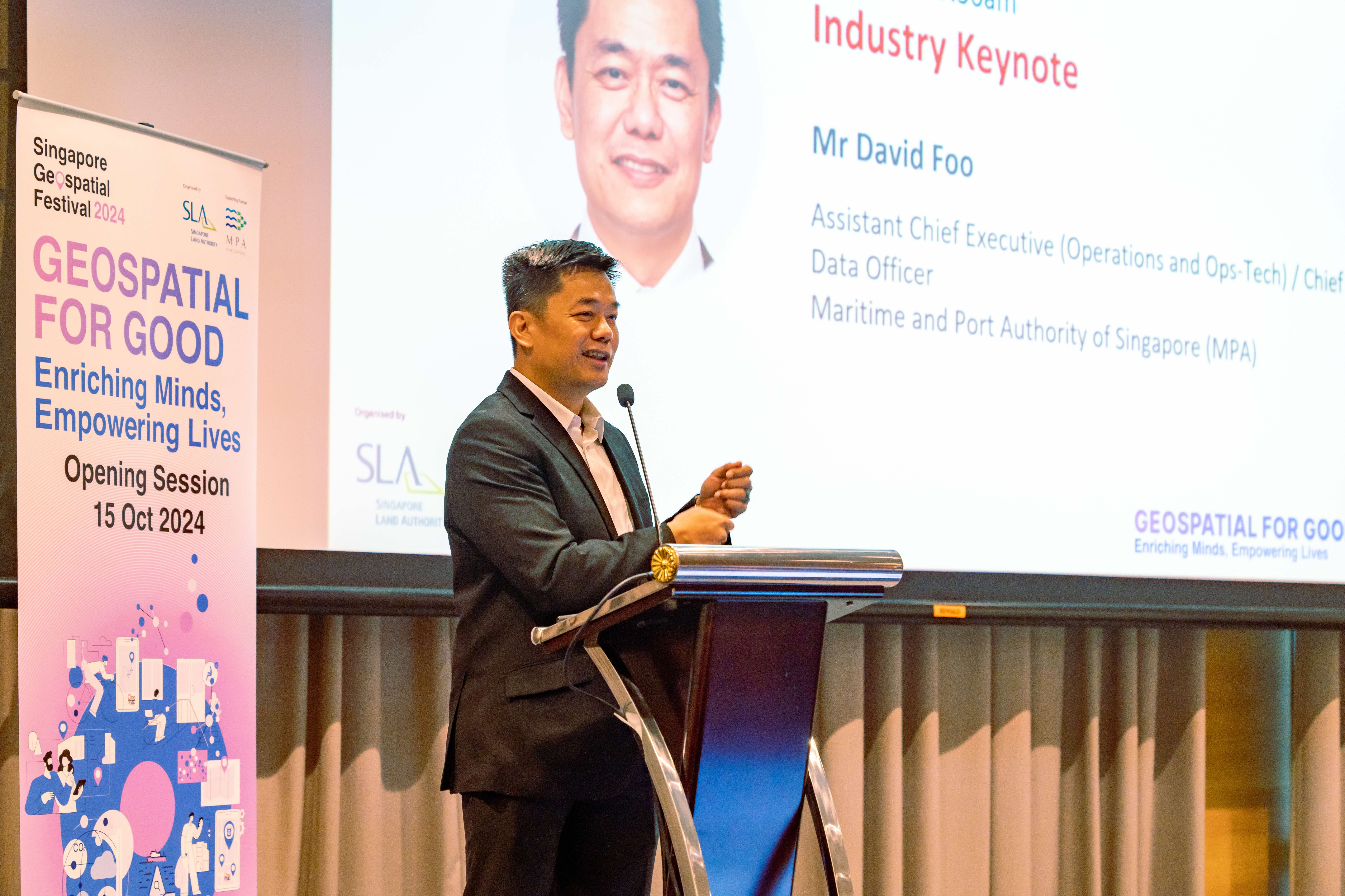 Man in dark suit speaks at podium during Singapore Geospatial Festival 2024 Industry Keynote by Mr David Foo.