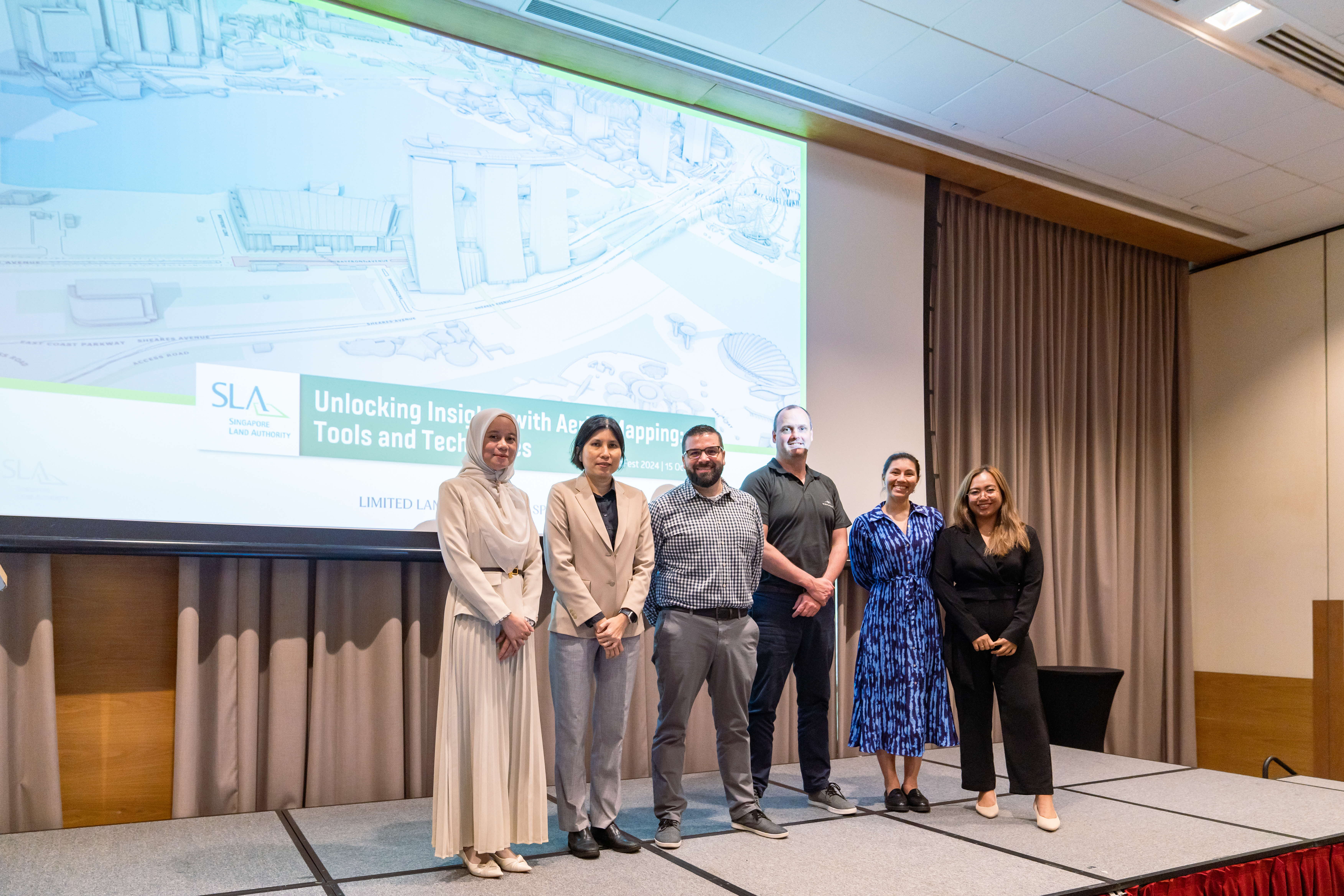 Six people stand on a stage in front of an SLA presentation slide about aerial mapping tools.