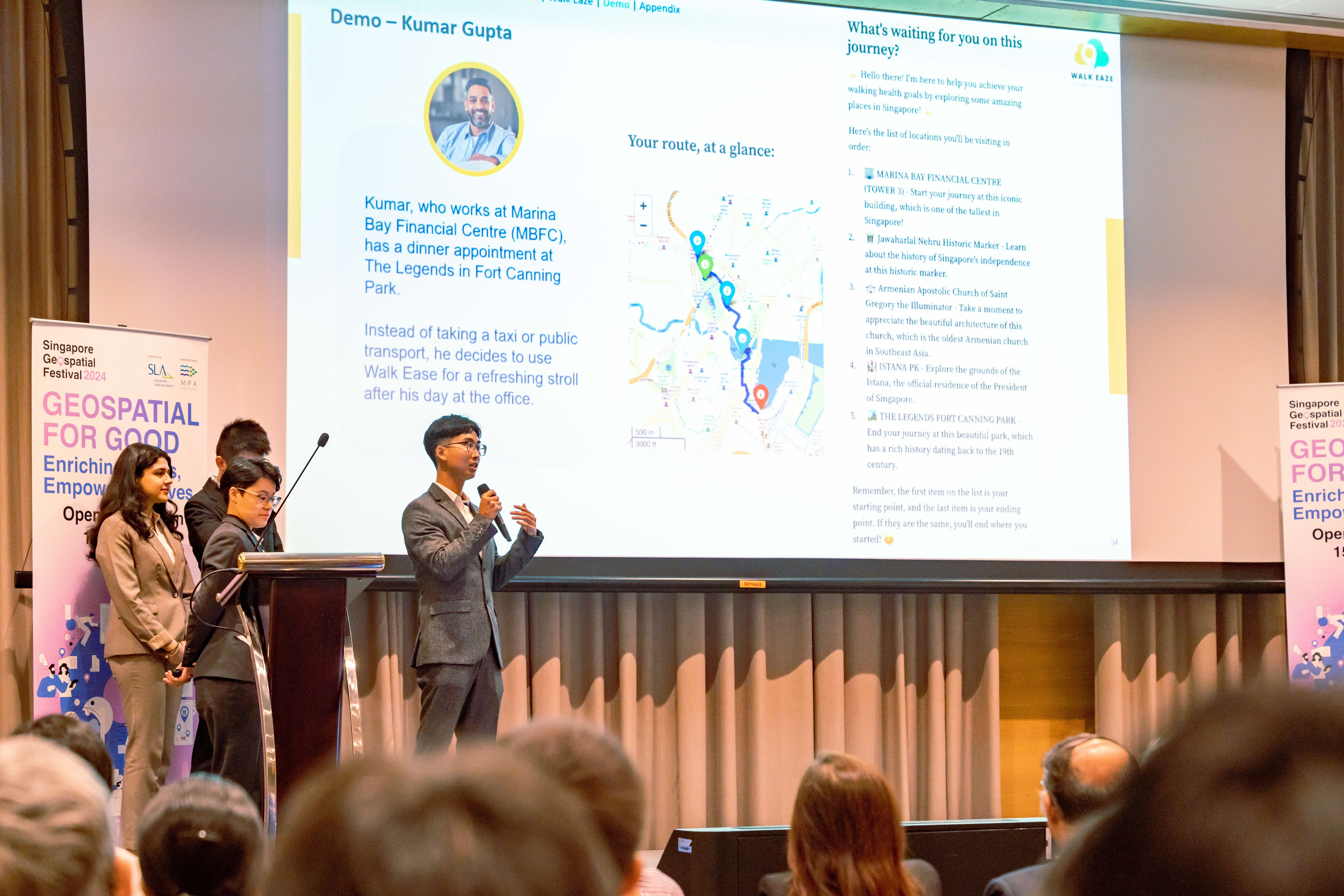 Three presenters on stage at Singapore Geospatial Festival 2024, with a Walk Eaze app demo slide projected behind them.