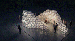 Arch of glowing white boxes with people gathered around in darkness