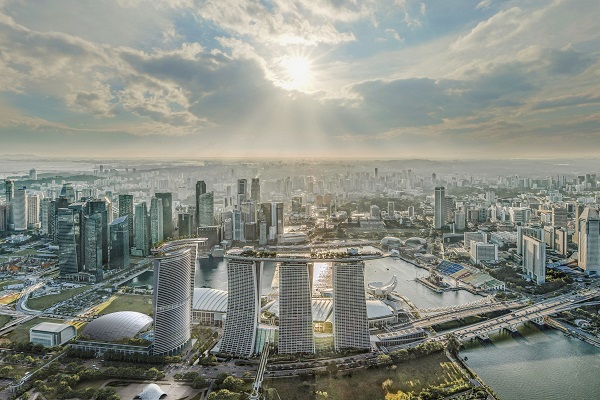 Aerial view of Singapore skyline with Marina Bay Sands under a bright, cloudy sky.