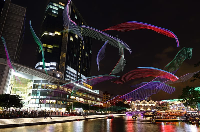 Singapore River at night with colorful light art installations above the water and buildings reflecting in the river.