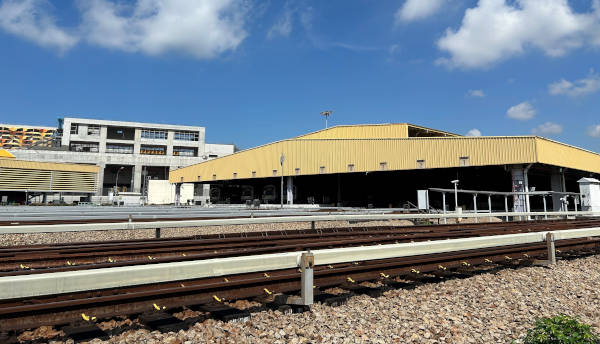 Train tracks leading to a station building under a blue sky.