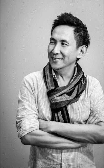 Black and white portrait of a smiling man with arms crossed, wearing a striped shirt and scarf.