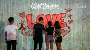 People pose before a graffiti wall with glowing "LOVE" at Light Singapore