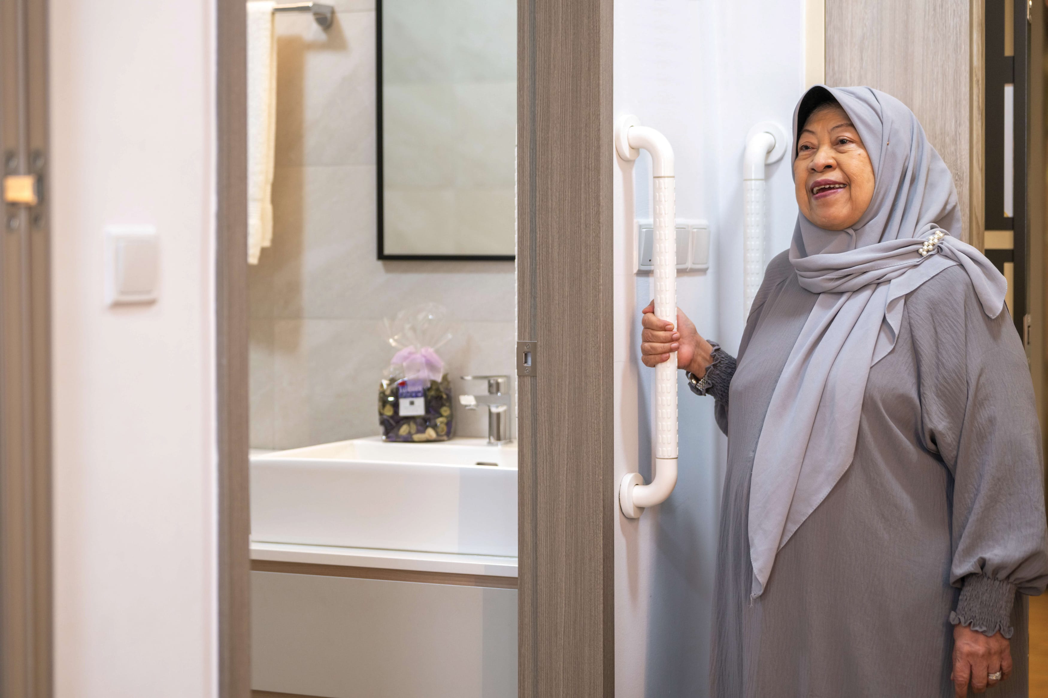 An older woman in a hijab uses a grab bar in an accessible bathroom.