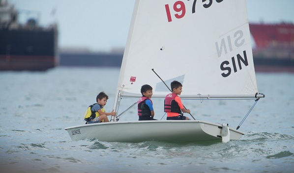 Three children wearing life vests sail a small sailboat on the water.