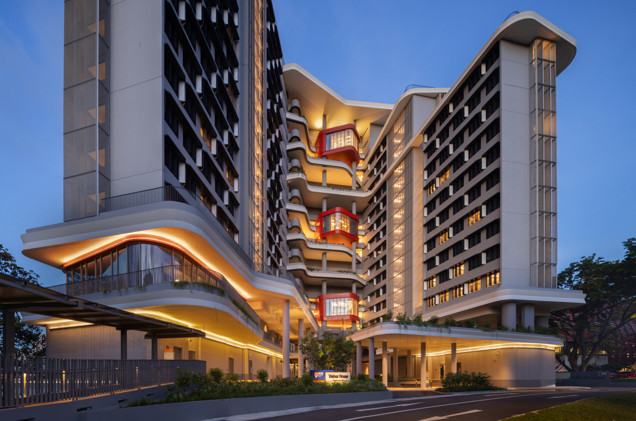 Exterior view of Valour House at dusk, showing modern architecture with layered balconies and red accents.