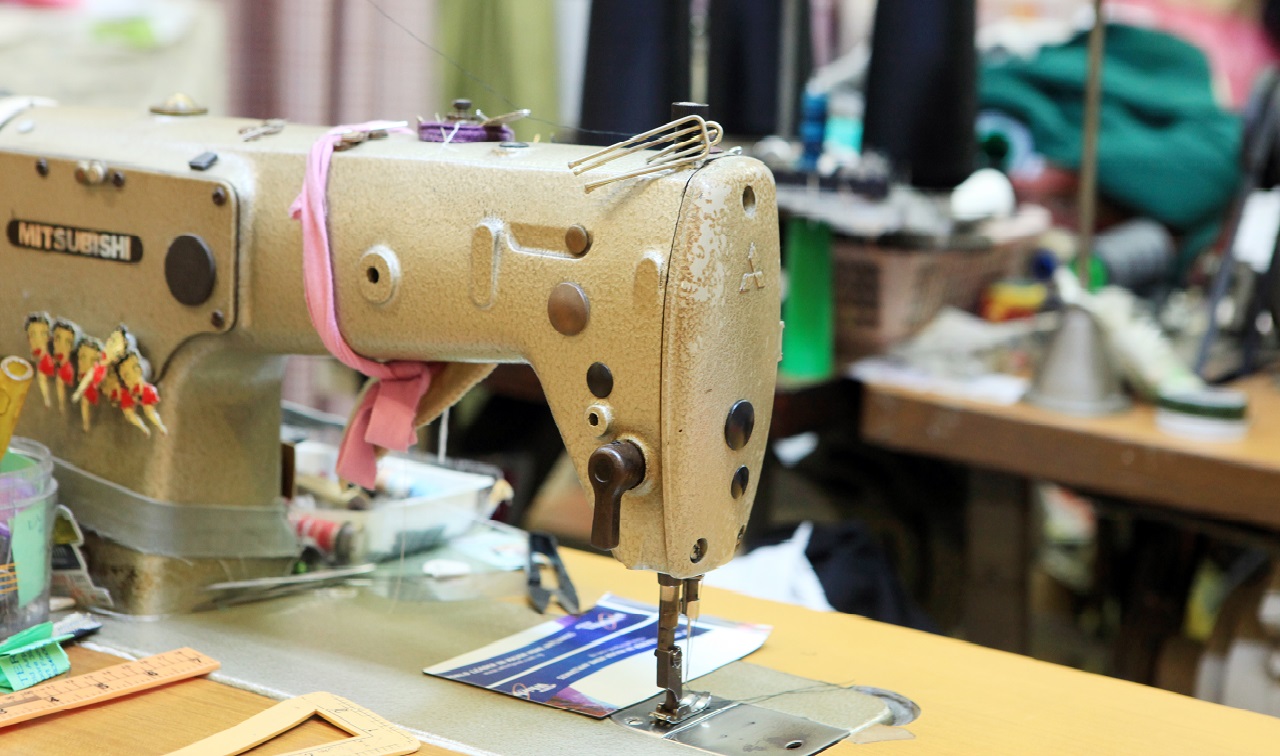 Close-up of a vintage sewing machine on a cluttered workbench in a tailor shop.