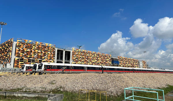 A train is parked in front of a building with a patterned facade against a blue sky with clouds.