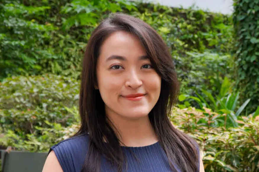Zann Tay, URA Scholar, smiling outdoors against a green leafy backdrop