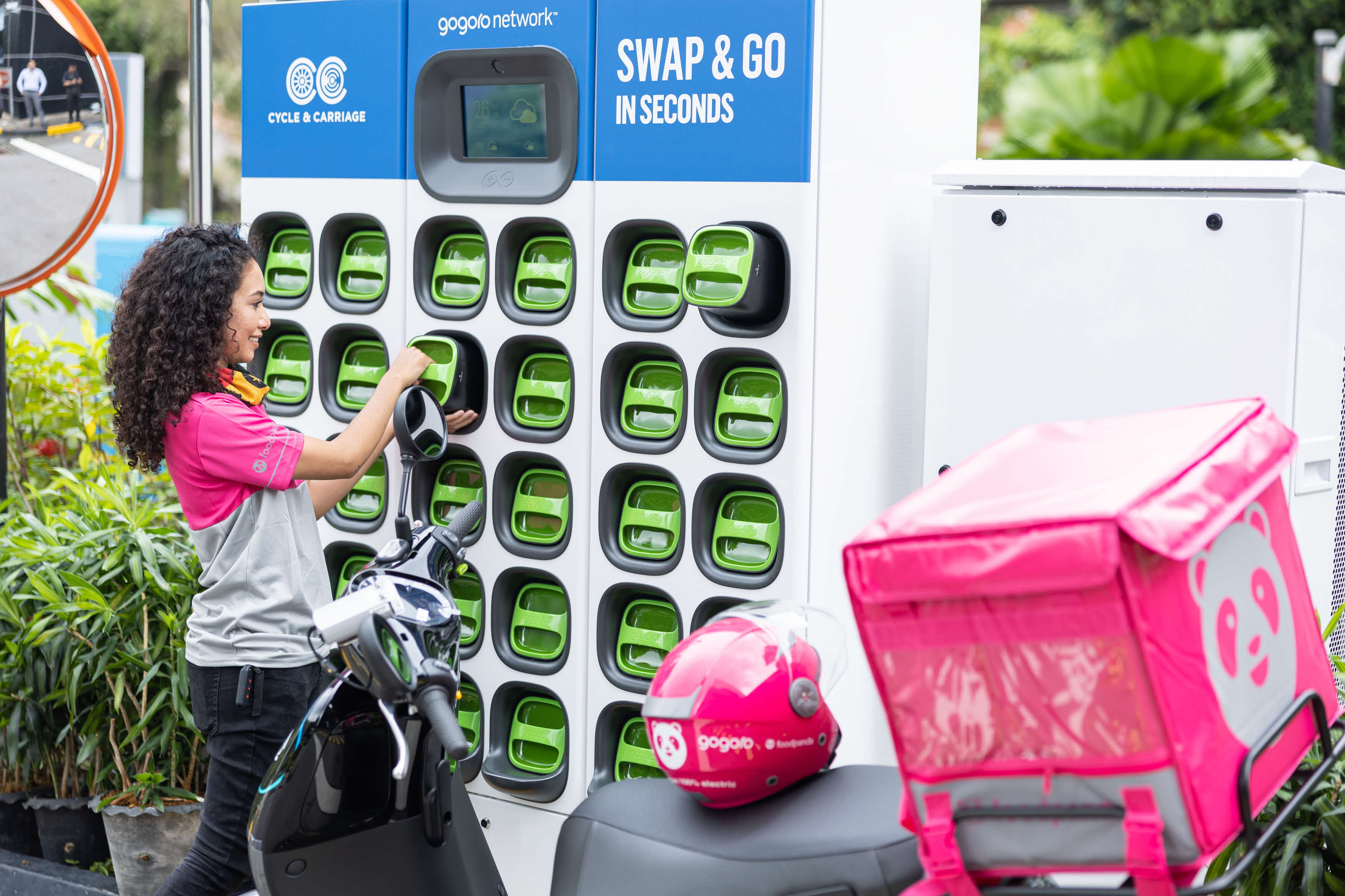 Delivery rider swapping scooter batteries at a Gogoro battery station.