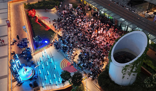 Aerial view of a concert with a large crowd, stage lights, and unique architecture at night.