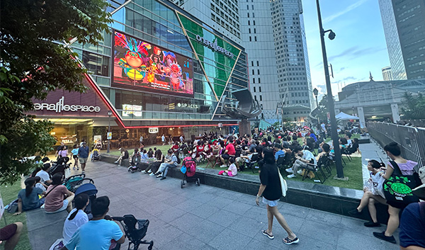 Outdoor film screening in Raffles Place, Singapore. People are watching a large screen on a building facade.