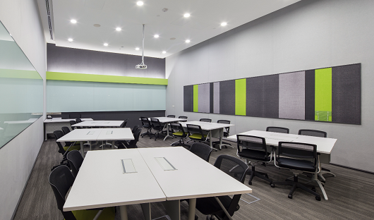 Classroom with white tables and black chairs. A projector hangs from the ceiling.