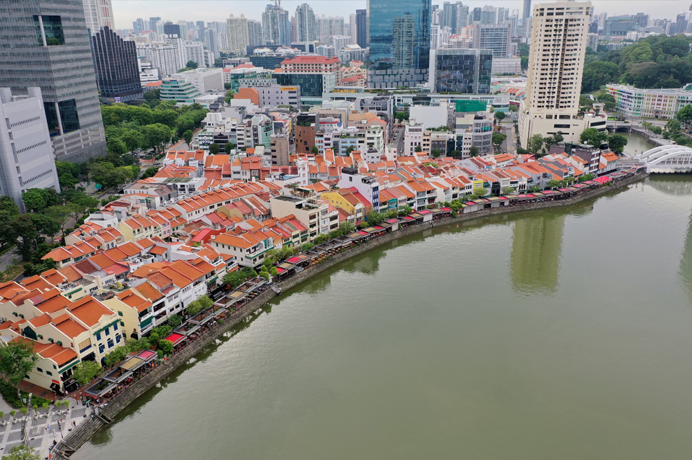 Aerial view of riverfront buildings with red tile roofs in a city, with skyscrapers in the background.