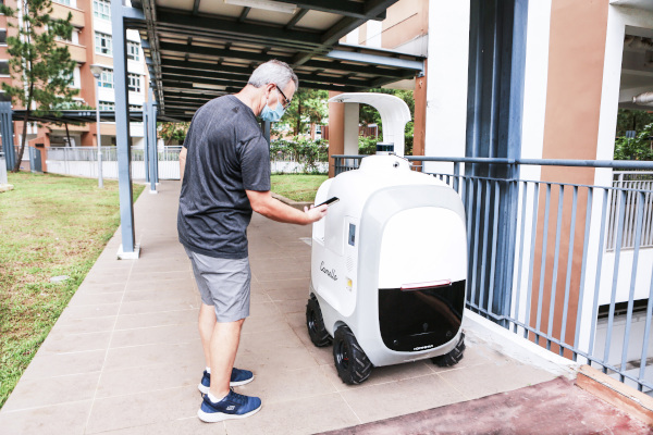 A masked man interacts with a delivery robot on a covered walkway.