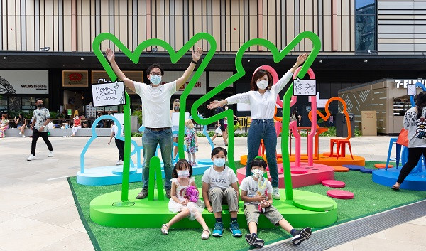 A family wearing masks posing at a colorful public art installation in an outdoor plaza.