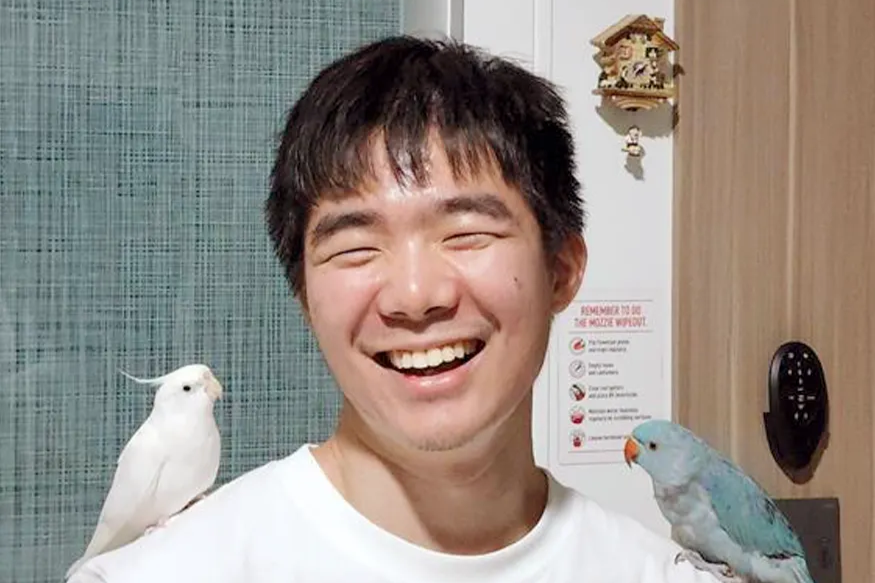 Joash Chin, URA Scholar, smiling with two pet birds perched on his shoulders