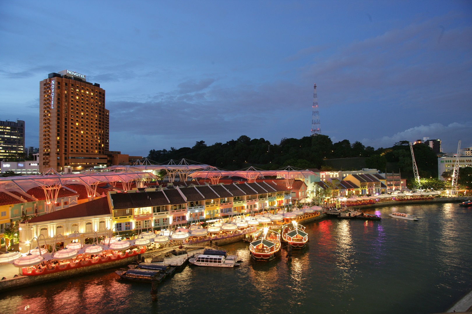 Night view of Clarke Quay with brightly lit restaurants and boats along the river.